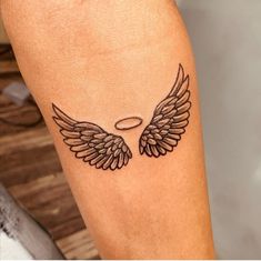 a tattoo on the leg of a person with an angel wing and halo above it