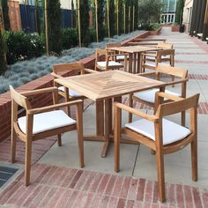 there are many wooden chairs and tables on the sidewalk near each other, with white cushions