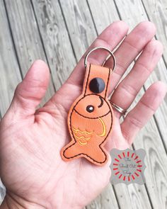 a hand holding an orange key chain with a fish on it's face and eyes