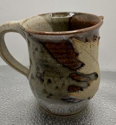 a coffee cup with a leaf on it sitting on top of a silver countertop