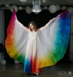 a woman in a white dress holding a rainbow colored shawl