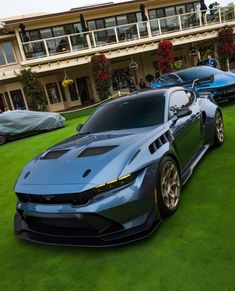 two blue sports cars parked in front of a large building on grass with people standing around