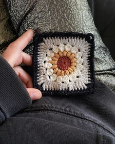 a hand holding a small crocheted square with a sunflower on the center