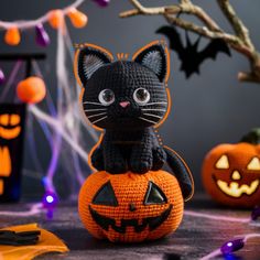 a crocheted black cat sitting on top of a pumpkin in front of halloween decorations