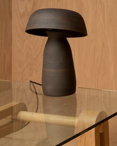 a wooden table with a glass top and a black lamp on the bottom, in front of a wood paneled wall