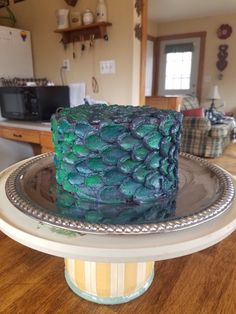 a blue and green cake sitting on top of a metal platter in a kitchen