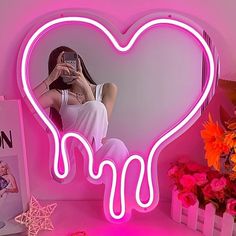 a woman taking a selfie in front of a neon heart