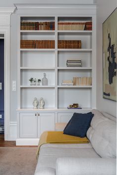 a living room filled with white bookshelves next to a couch and painting on the wall