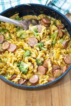 a skillet filled with pasta, sausage and broccoli on top of a wooden table