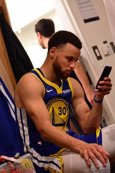 a man sitting on the floor looking at his cell phone while wearing a basketball uniform