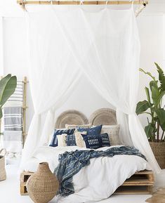 a bed with white linens and pillows in a room next to potted plants