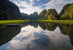 a small boat floating on top of a river next to tall green mountains under a blue sky