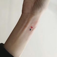 a small heart tattoo on the wrist is shown in red and black ink, with two hearts