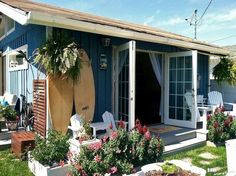 a blue house with surfboards on the porch and flowers growing in pots next to it