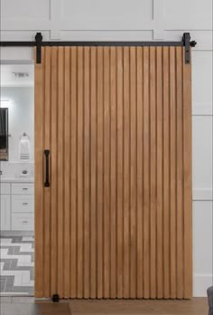 a wooden sliding door with black hardware on the top and bottom bars, in front of a white kitchen