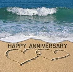 two hearts drawn in the sand with happy anniversary written on it and wave coming in