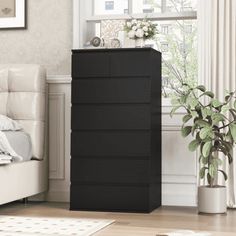 a black chest of drawers in a living room next to a white couch and potted plant