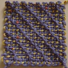 a close up of a knitted object on a white surface with yellow and blue yarn