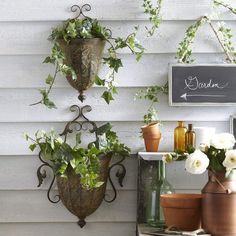 three hanging planters with white flowers and greenery on the side of a house