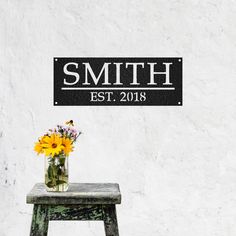 a vase filled with yellow flowers sitting on top of a wooden stool next to a white wall