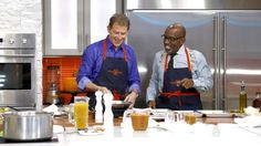 two men in aprons are preparing food on a kitchen counter with an orange and white sign