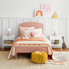 a bedroom with white walls and pink bedding, yellow foot stools and rug