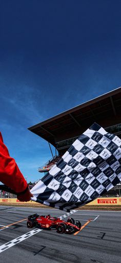 a red race car driving past a giant checkered flag on the side of a racing track