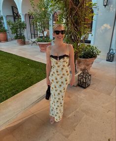 a woman standing in front of a house wearing sunglasses and a dress with sunflowers on it