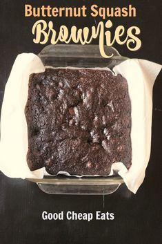 a chocolate brownie in a glass dish with white paper on the bottom and words butternut squash brownies good cheap eats