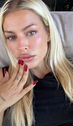 a woman with long blonde hair and red nails laying on a bed looking at the camera