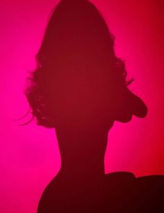 the silhouette of a person's head in front of a pink background with red light