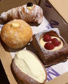 four pastries in a box with powdered sugar, raspberries and cream