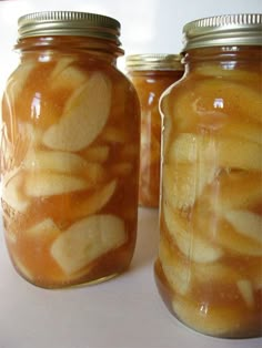 three jars filled with apple slices sitting on top of a white countertop next to each other