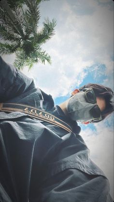 a man wearing sunglasses and a hoodie is standing under a tree with the sky in the background