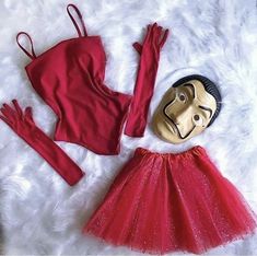 a red dress and mask are laying on a white furnishing next to a gold mask