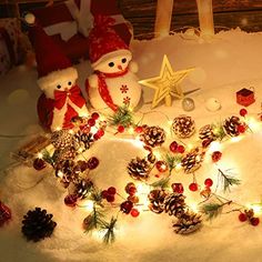 two teddy bears sitting in the snow next to pine cones and christmas decorations with lights on them