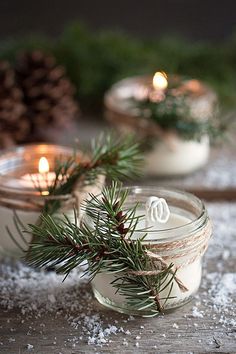 two mason jars filled with candles sitting on top of snow covered ground next to pine cones