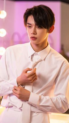 a young man in a white suit adjusting his tie