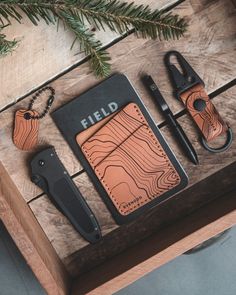 the contents of a leather tool kit laid out on a wooden table with pine branches