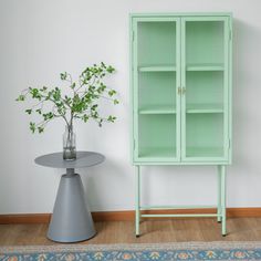 a green cabinet next to a small table with a vase on it and a plant in the corner