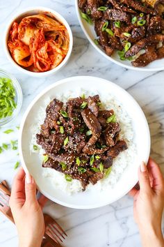 someone is holding a plate with rice and meat on it next to bowls of vegetables