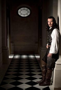 a man dressed in period clothing standing on a checkered floor with a clock behind him