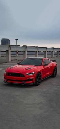 a red sports car parked in a parking lot next to some concrete pillars and an overcast sky