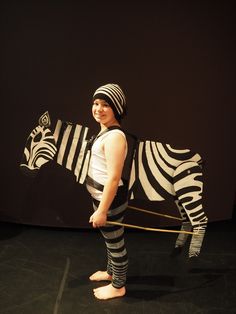 a young boy is standing next to a zebra statue that has been made out of cardboard