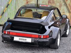 a black porsche parked in front of a rusted metal wall with the door open