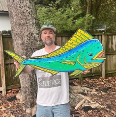 a man holding up a large fish shaped cardboard cutout in front of a tree