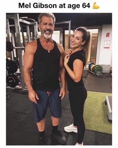 a man and woman posing for a photo in front of a gym equipment area with the caption, mel gibson at age 64