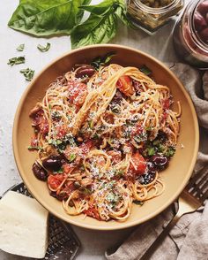 a bowl filled with pasta and olives on top of a table next to cheese