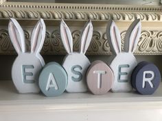 three ceramic easter bunnies sitting on top of a mantle next to the word easter