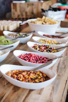 many bowls filled with different types of food on a wooden table in front of other dishes